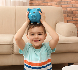 Young boy smiling while holding a blue piggy bank on his head.
