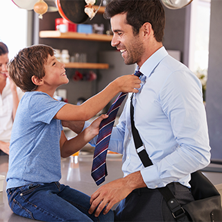 young son sitting on counter helping dad straighten tie