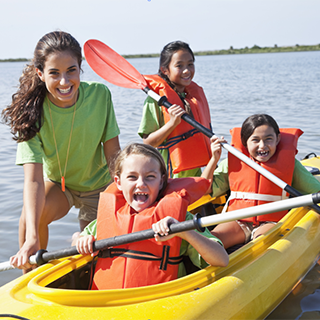 adult helping children kayak on a lake