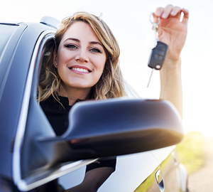 Young woman sitting in her car smiling while holding keys to her new car in her hand,